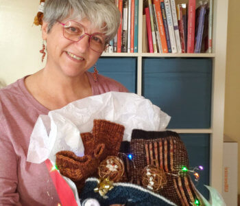 Brenda holding up a gift box with finished knits in it
